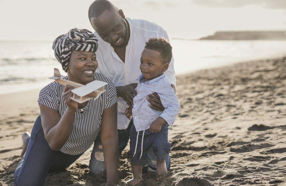 Happy african family having playful time on the beach - Family love - Parents and toddler outdoor